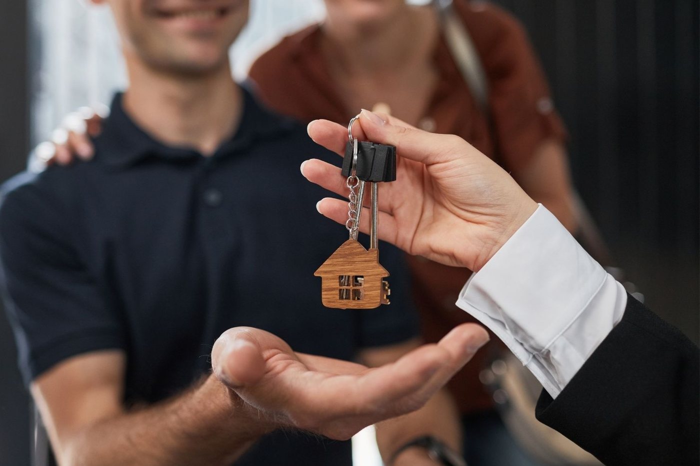 A real estate professional handing house keys on a wooden house keyring to a smiling couple.
