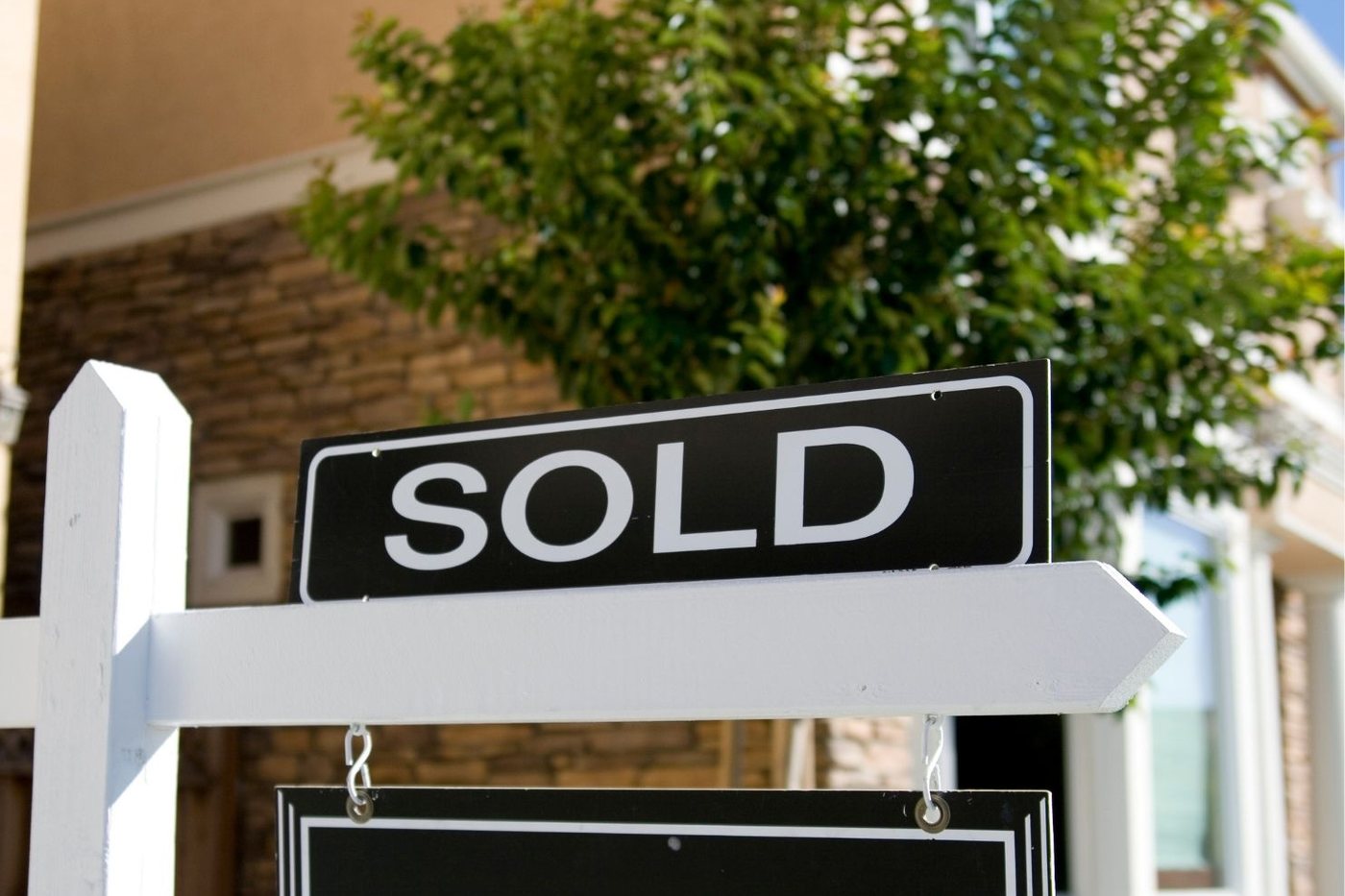A black and white SOLD sign on a post in front of a home.